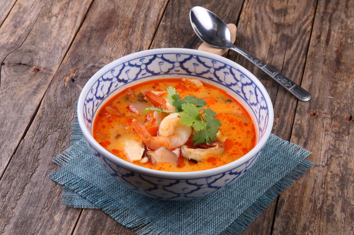 A close-up shot of spicy Thai Tom Yum noodles with large shrimp and lime slices.