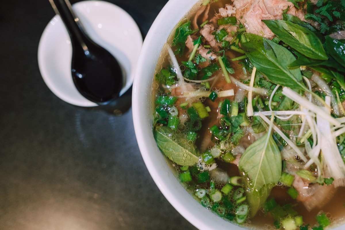Tigela de macarrão vietnamita com caldo claro e ervas verdes.