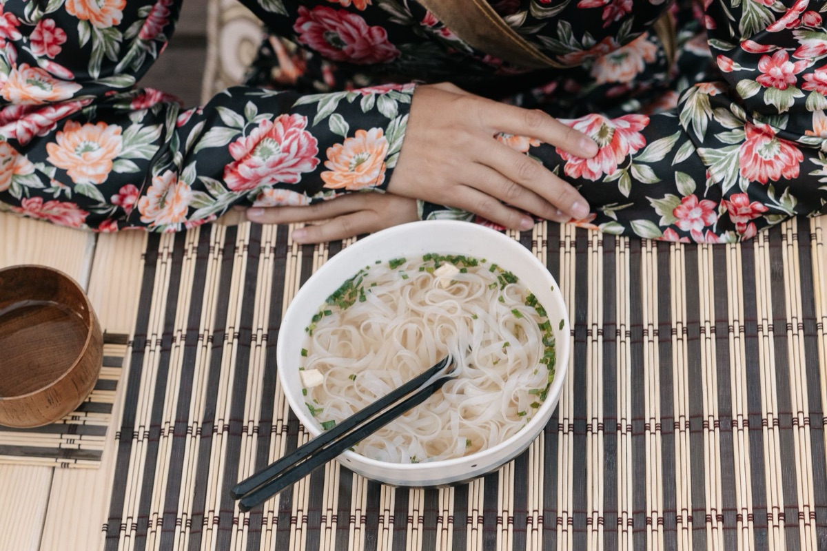 Una persona sosteniendo un vaso de ramen con palillos de madera.