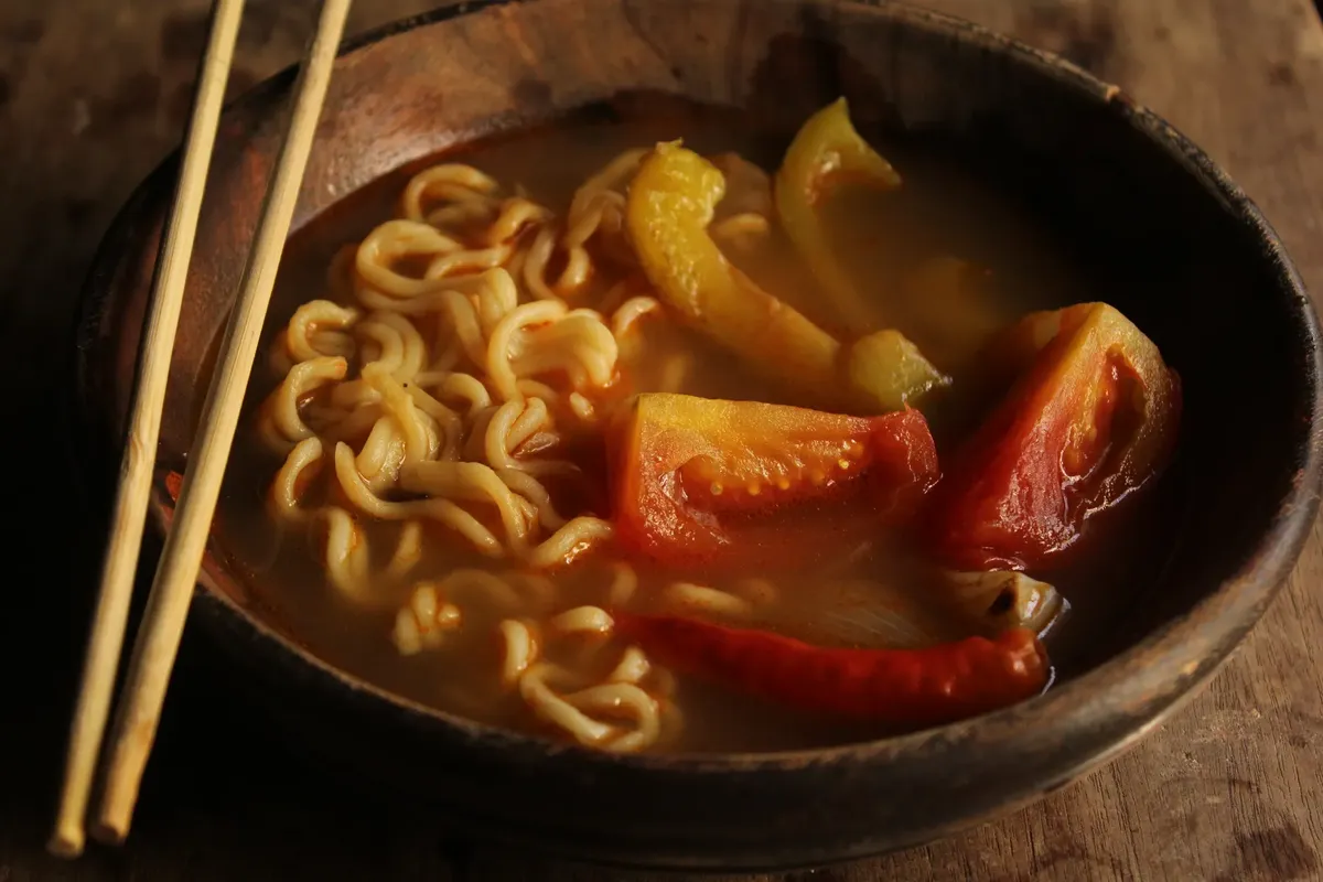Bowl of savory ramen noodle soup with tomatoes and peppers.