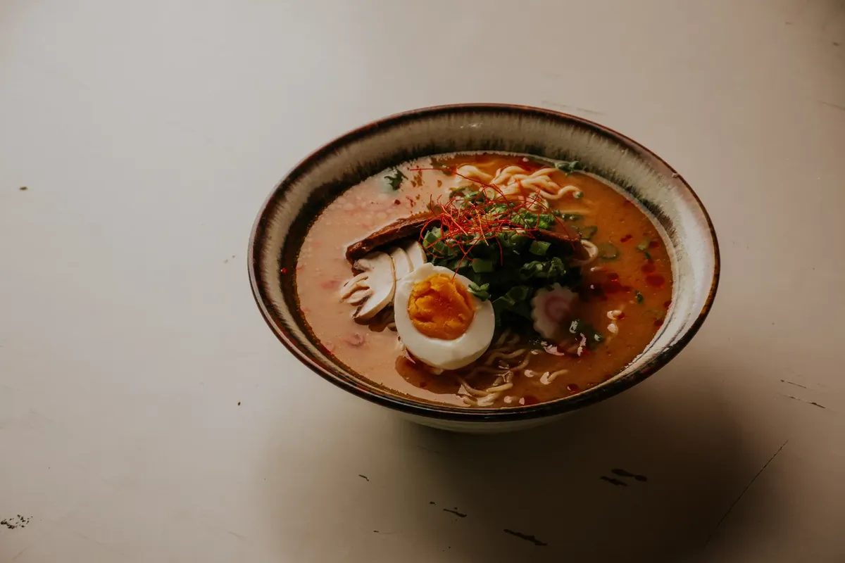 Appetizing ramen noodle soup with a soft-boiled egg, herbs, and spices in a ceramic bowl.