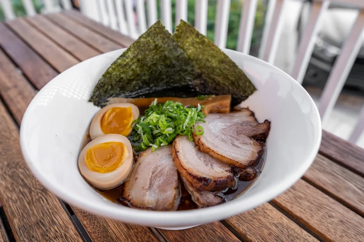 Appetizing bowl of traditional Japanese ramen with chashu, eggs, and nori on a wooden table.